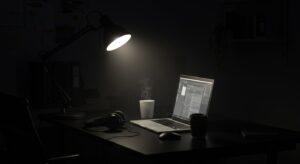 Dark themed night office with glowing laptop, ambient desk lamp, headphones, Pixlelo.com Variation 86