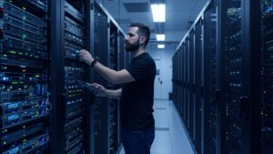 Male engineer in data center adjusting server rack with glowing ambient lights — clean high tech background, no text or dashboard visible by pixlelo.com Variation 04